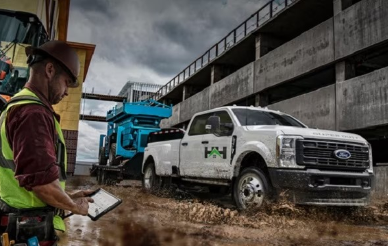 Construction worker using a tablet beside a Ford Super Duty truck at an active construction site.